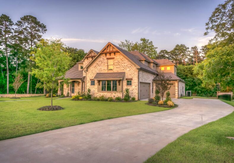 Elegant stone family home surrounded by trees, lush lawn, and vibrant garden.